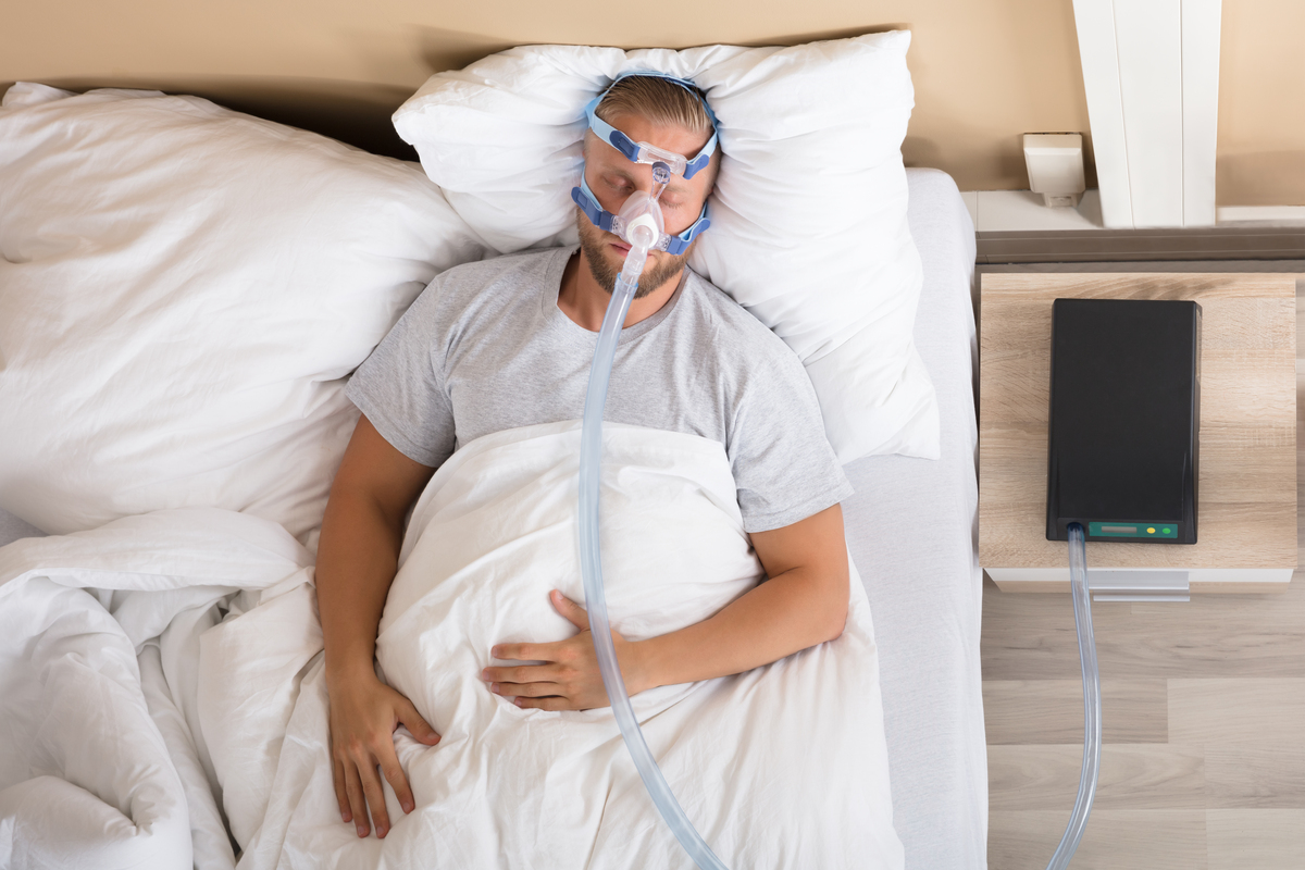 Young man lying on bed with sleep apnea continuous positive airway pressure (CPAP) machine