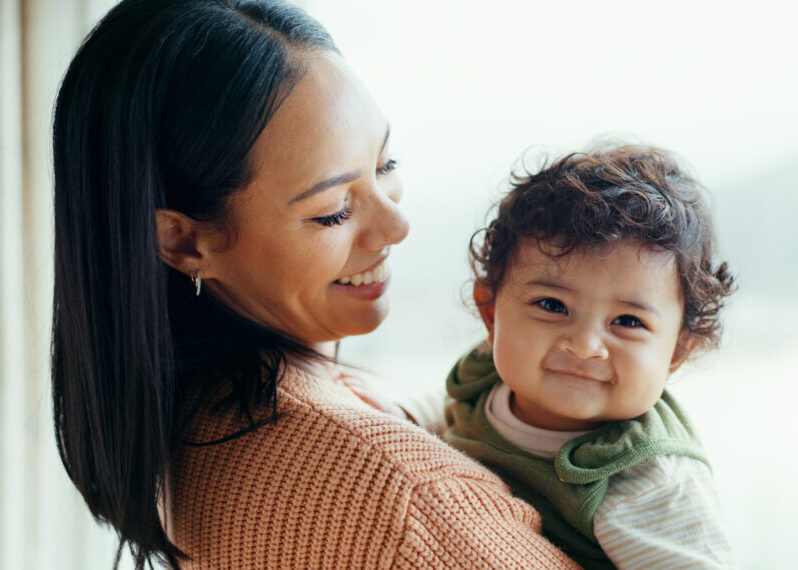 Mother, newborn and smile by window, home and happy together with care, love and bonding in childhood. Mom, infant baby and excited with connection, development and hug at family house in Canada