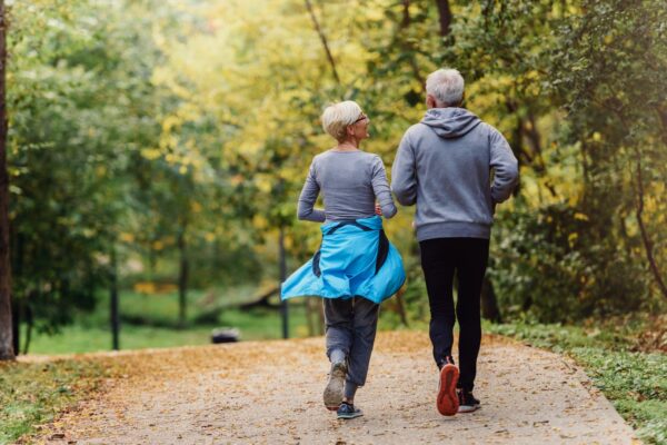 elderly couple, woman and man, wearing grey athletic wear running in woods.