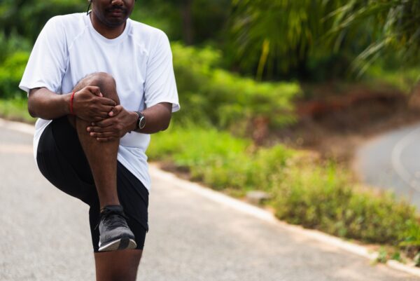 Young man wearing black shorts and white top stretching his knee