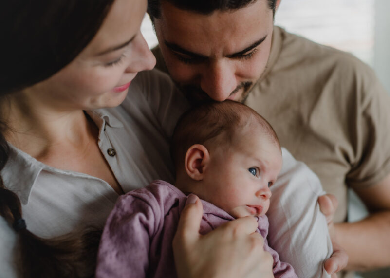 Close up of young parents holding and kissing their newborn baby indoors at home