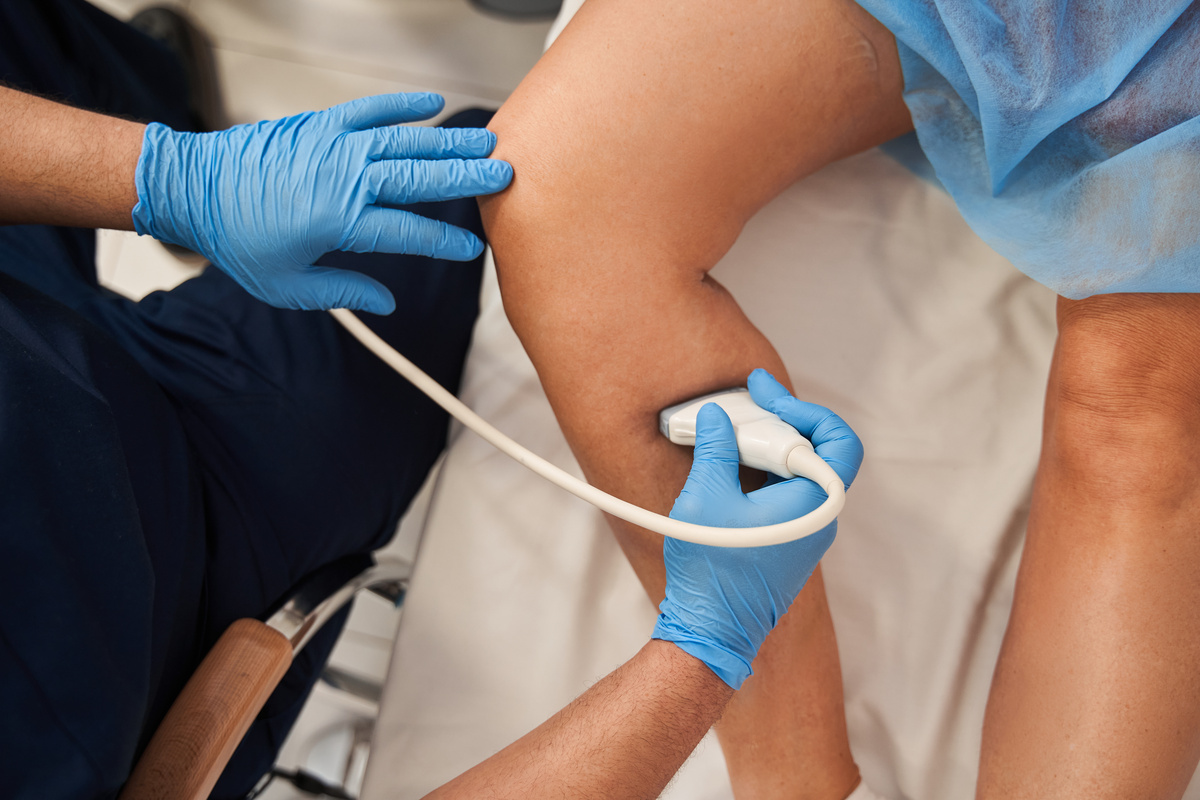 Doctor performing Doppler ultrasound scan on leg of patient
